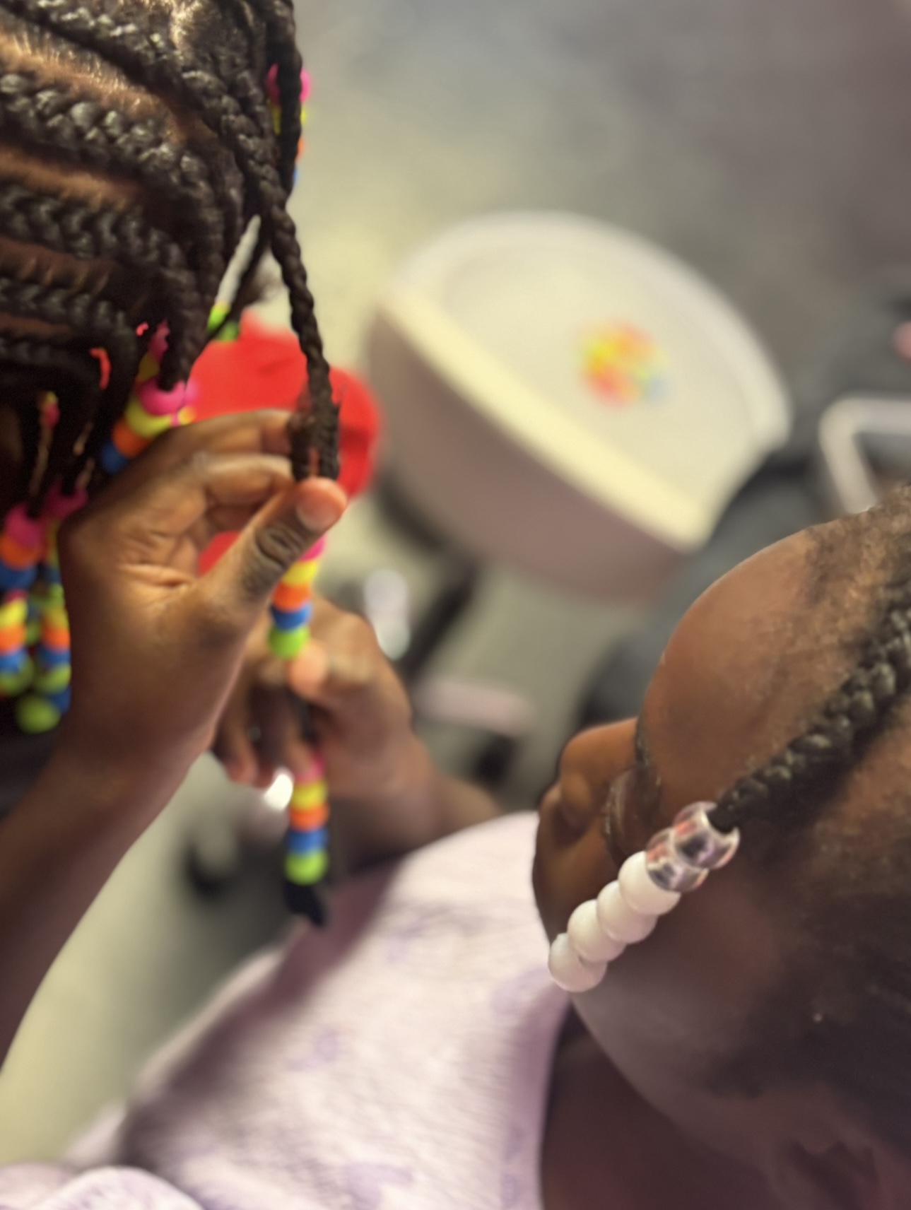 Stylist adding colorful beads to a child's braids at 360 Attitude Children's Salon